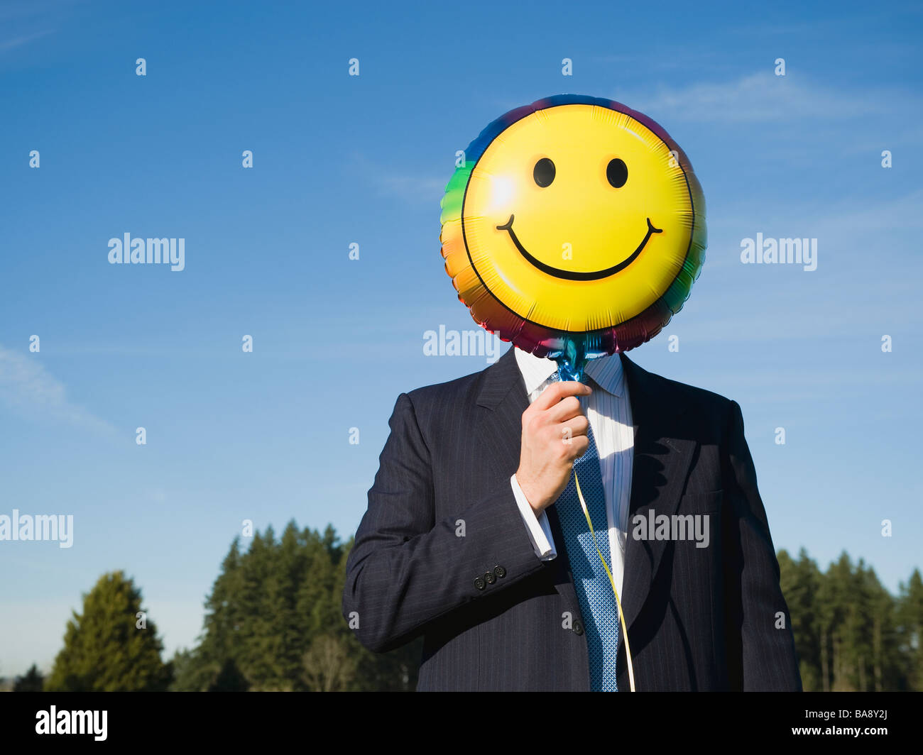 Businessman holding smiley face balloon over face Stock Photo