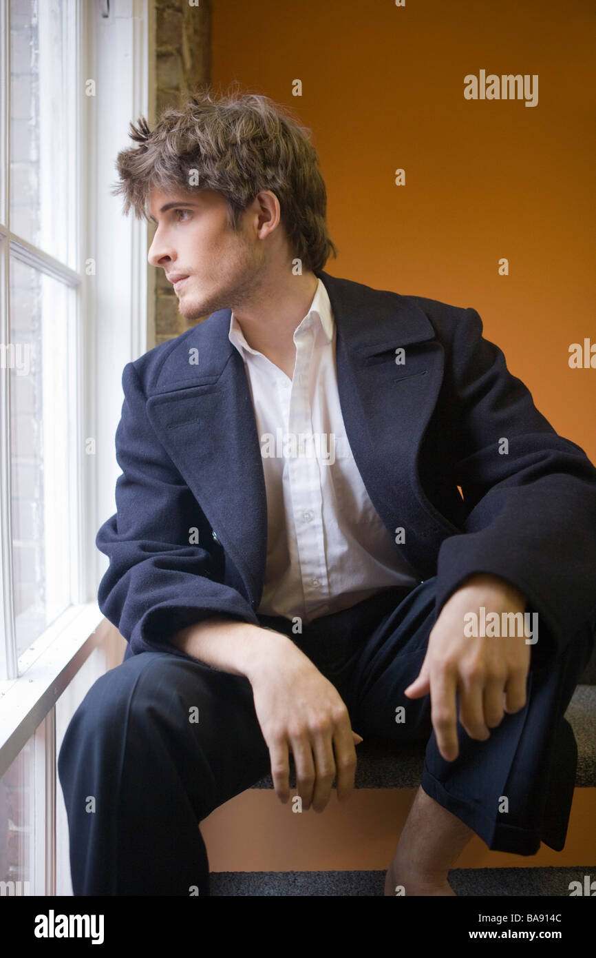 Portrait of young adult man sitting on stairs looking out window Stock ...