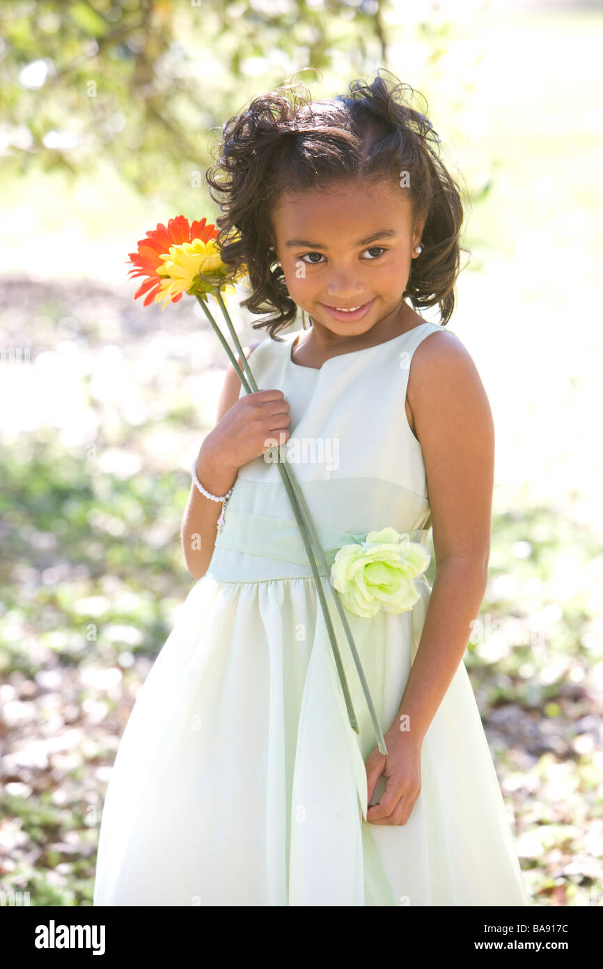 Portrait of African American girl in dress standing in park holding flowers Stock Photo
