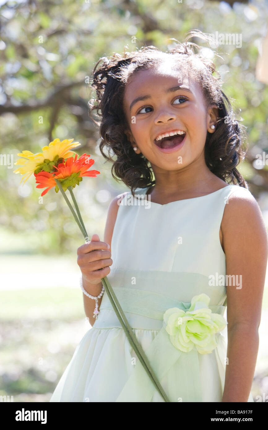Portrait of African American girl in dress standing in park holding flowers Stock Photo