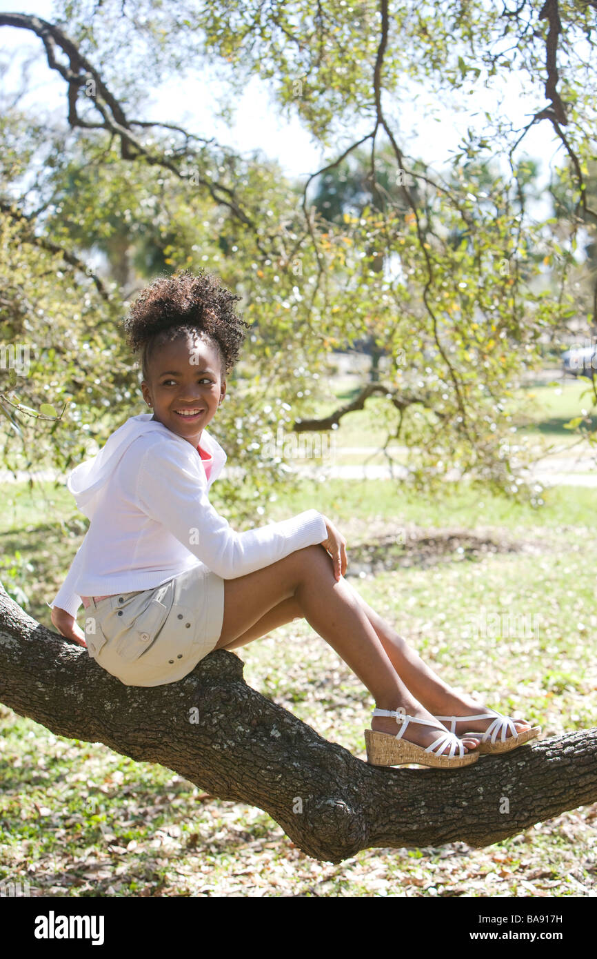 Portrait of African American girl sitting on tree branch in park Stock ...