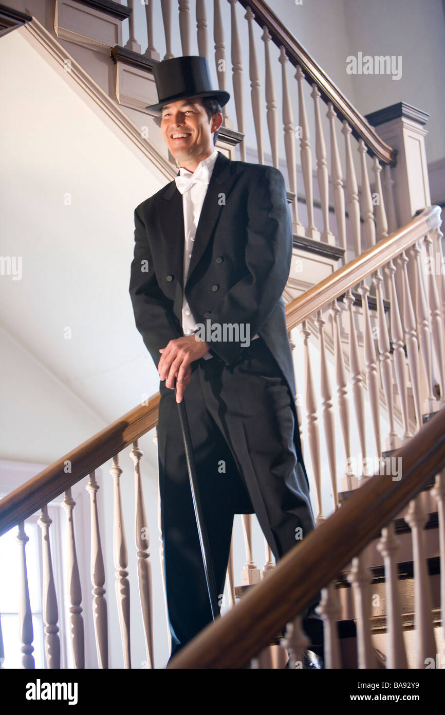 Asian man in tuxedo standing on stairs with top hat and cane Stock