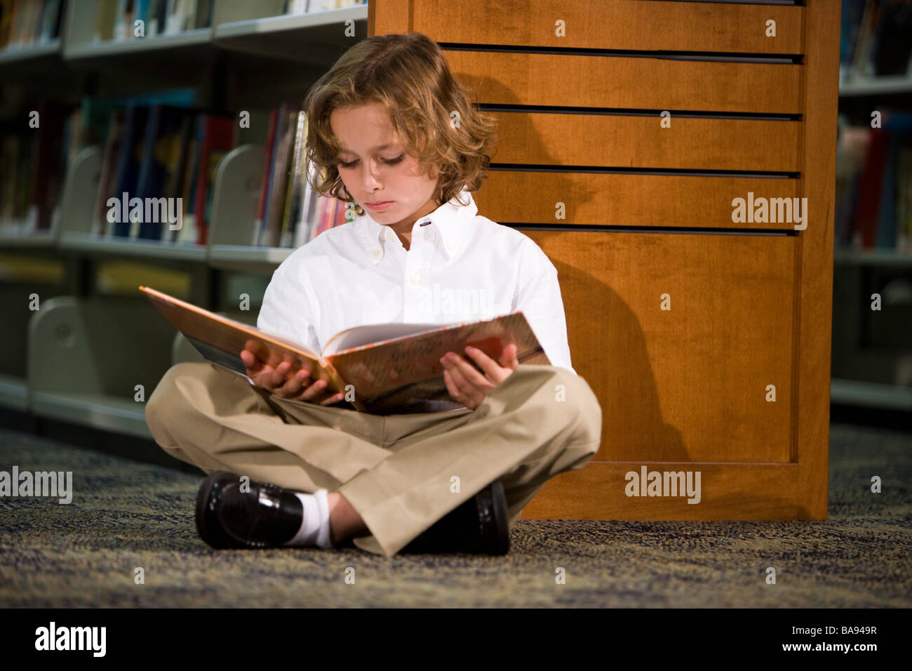 Elementary school boy sitting on library floor reading Stock Photo - Alamy