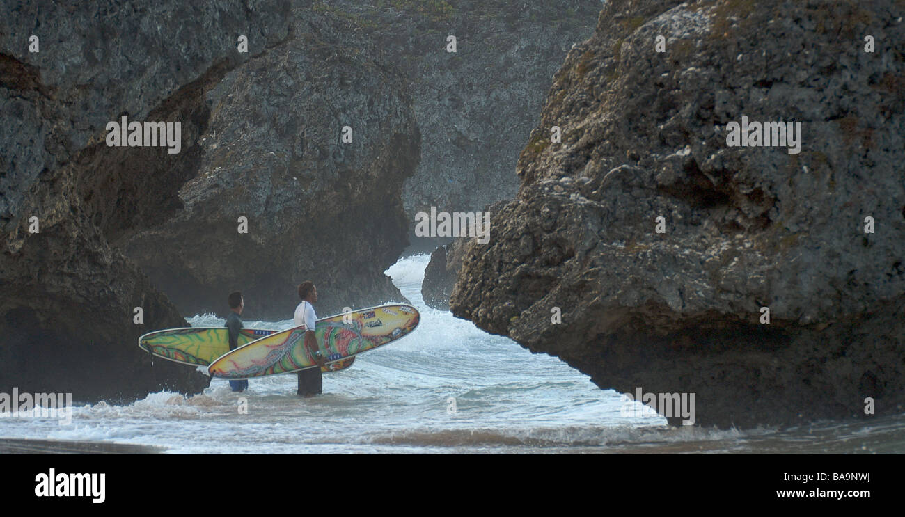 Two surfers hold their surfboards and check out the waves between rocks ...