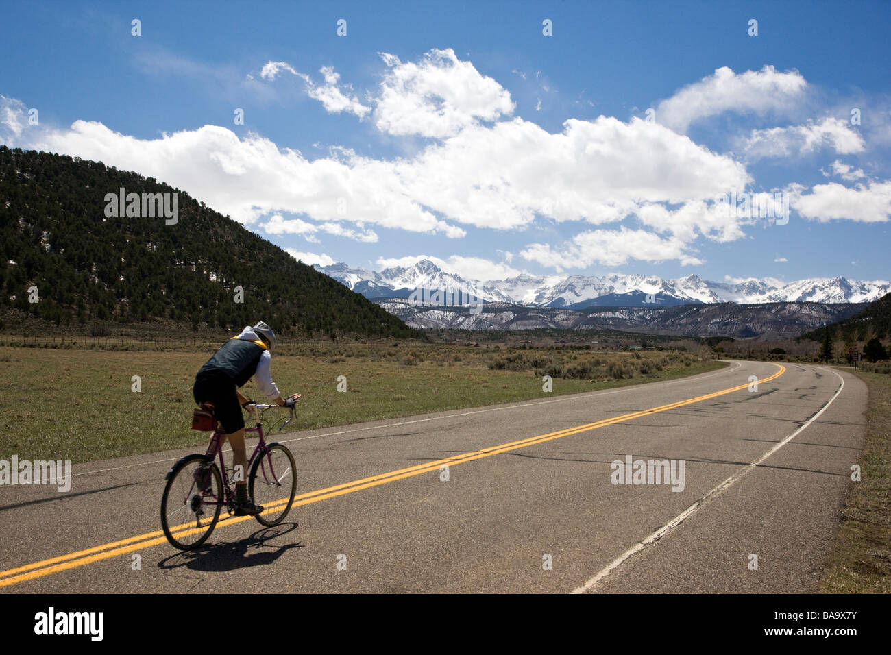 Bicyclist on a road in Ridgeway State Park near Ridgeway Colorado San Juan Mountains and Uncompahgre National Forest in distance Stock Photo