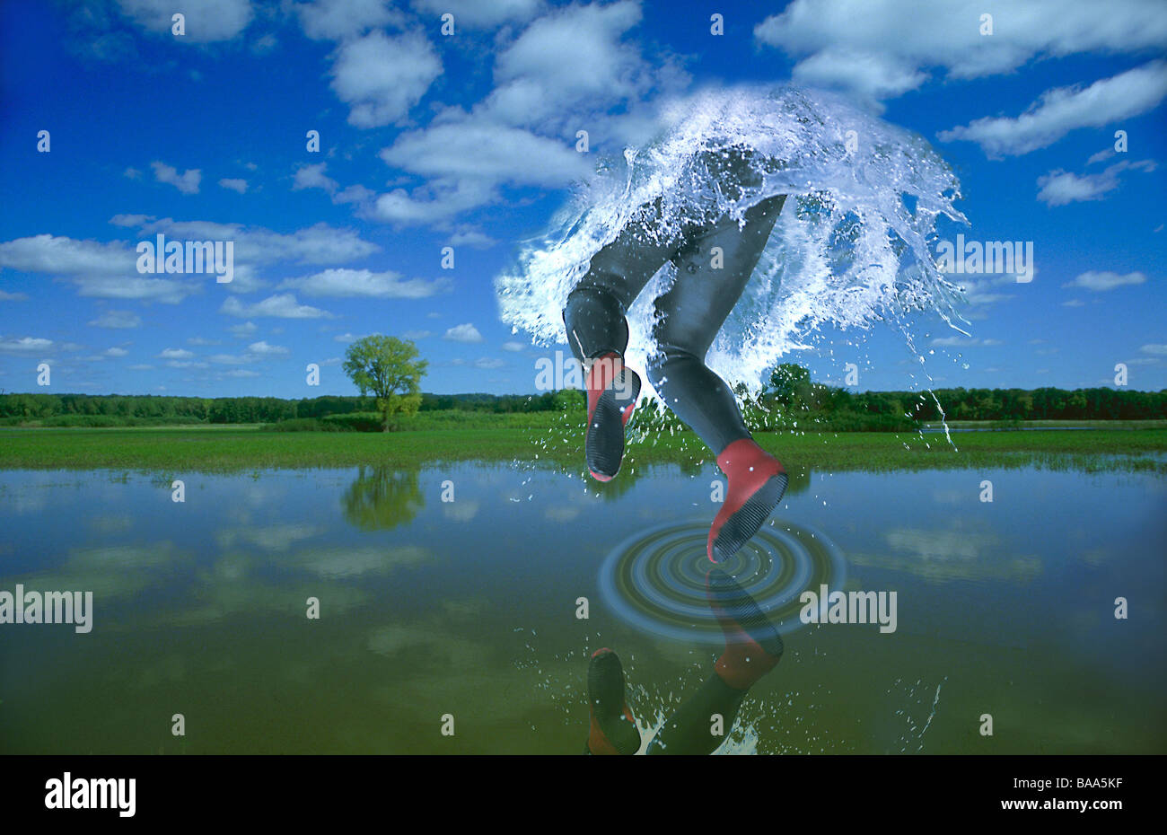 A diver makes a splash into the clouds and sky and creates a spiral in the lake below. Stock Photo