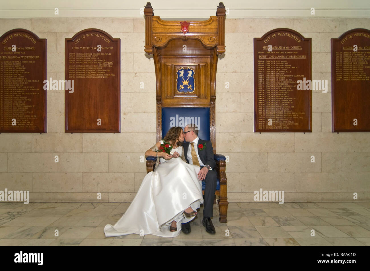 Horizontal wide angle portrait of newly wed bride and groom sitting together on a large formal throne style wooden chair Stock Photo