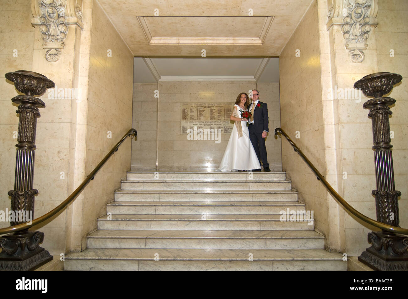 Horizontal wide angle portrait of the newly wed bride and groom posing for photographs on a large formal marble staircase Stock Photo