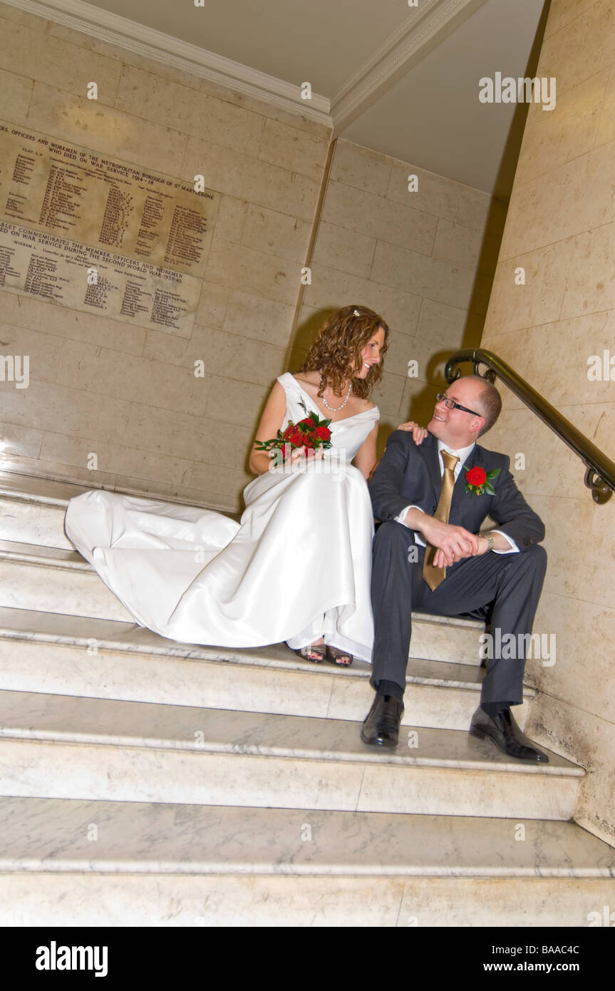 Vertical wide angle portrait of the newly wed bride and groom posing for photographs on a large formal marble staircase Stock Photo