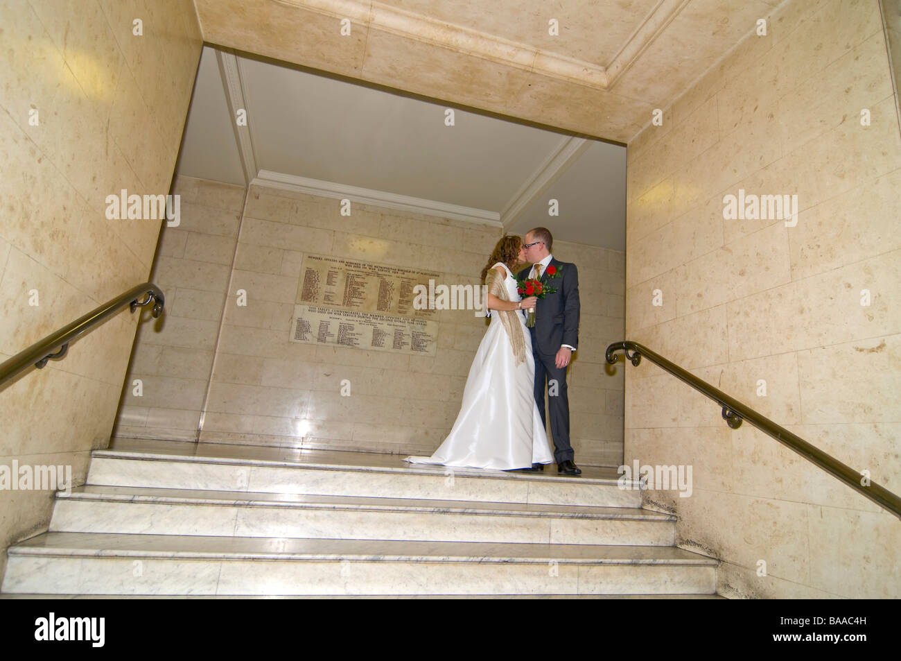 Horizontal wide angle portrait of the newly wed bride and groom posing for photographs on a large formal marble staircase Stock Photo