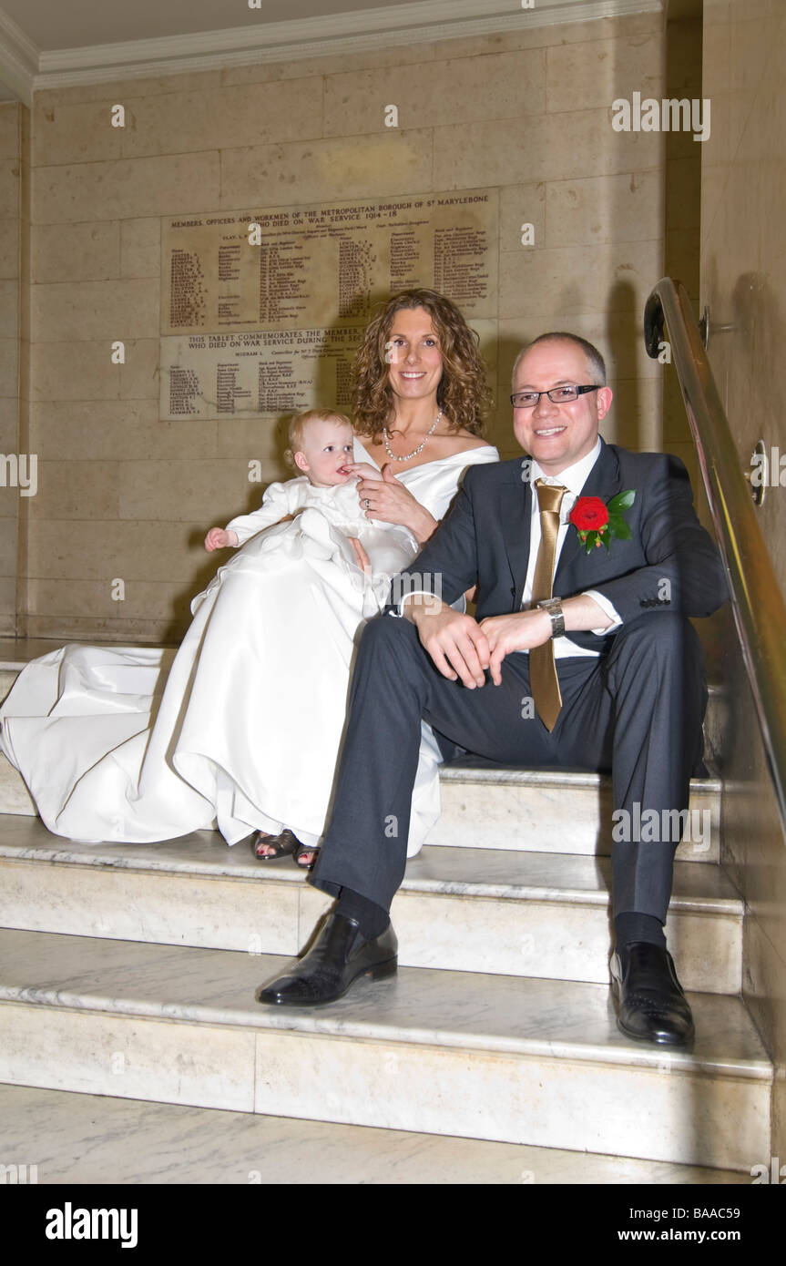 Vertical wide angle portrait of a newly wed bride and groom posing together for photographs with their baby daughter Stock Photo