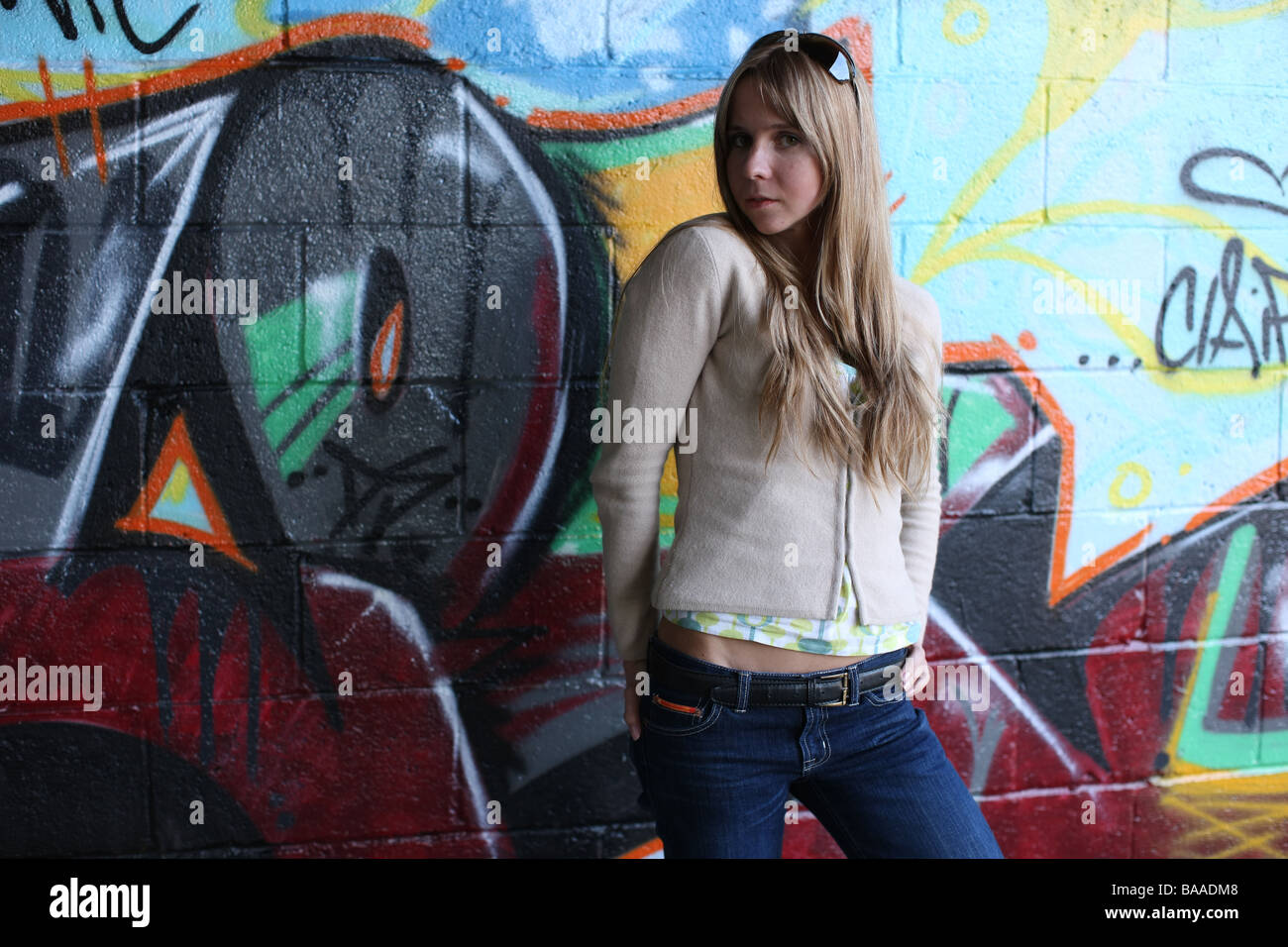 three quarter length shot of girl up against a graffiti sprayed wall Stock Photo