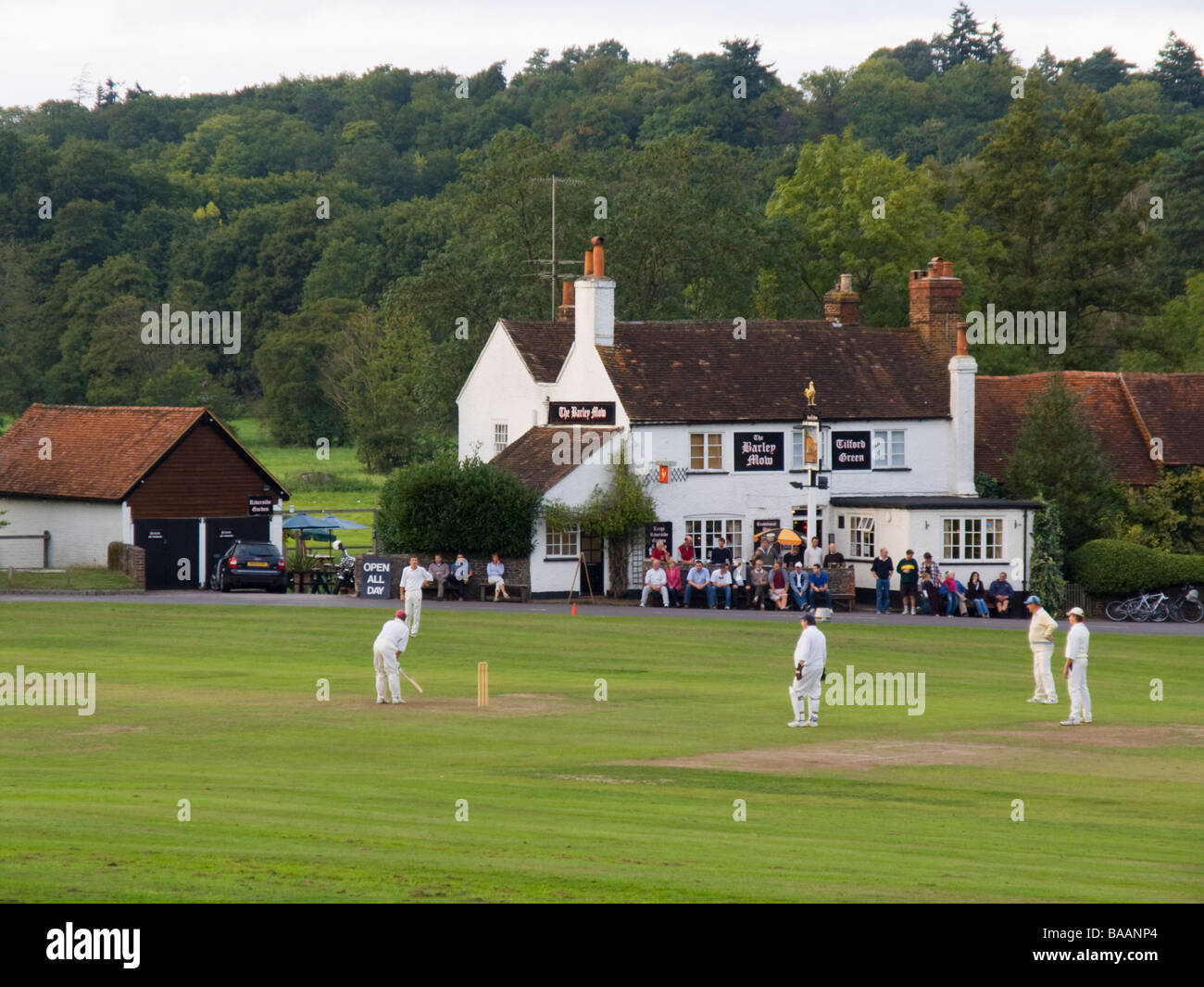 Playing cricket on a village green outside the Barley Mow country pub in summer. Tilford Surrey England UK Britain Stock Photo