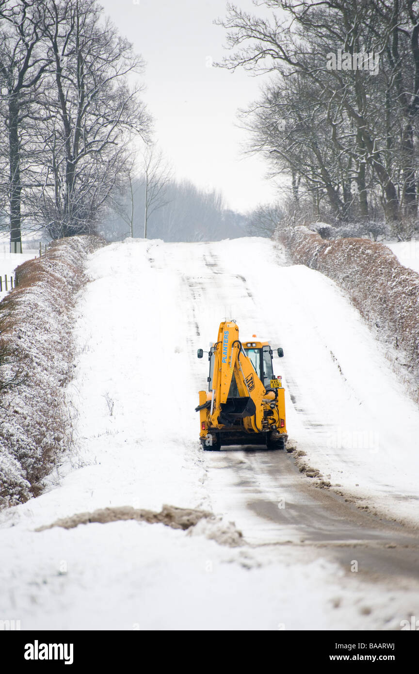 JCB being used to clear a snow covered road in the countryside in England at winter time Stock Photo
