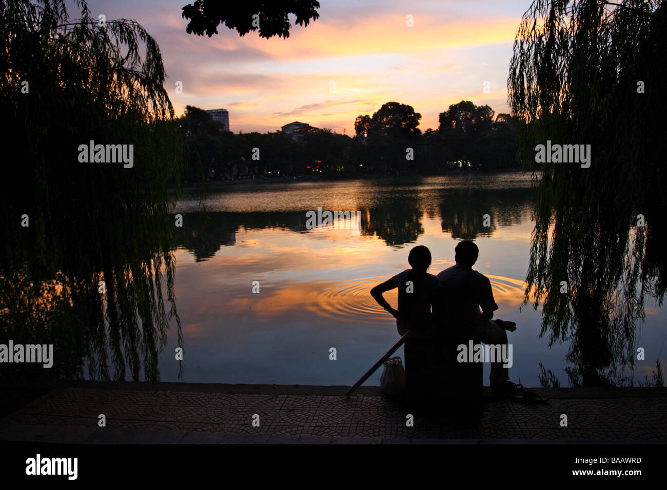Street scene. Couple sitting in front of a beautiful sunset on Hoan Kiem lake. Hanoi, Vietnam Stock Photo