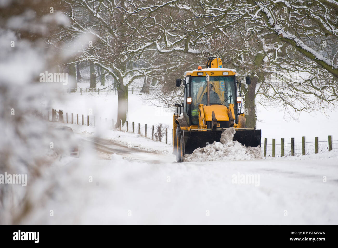 JCB being used to clear a snow covered road in the countryside in England at winter time Stock Photo