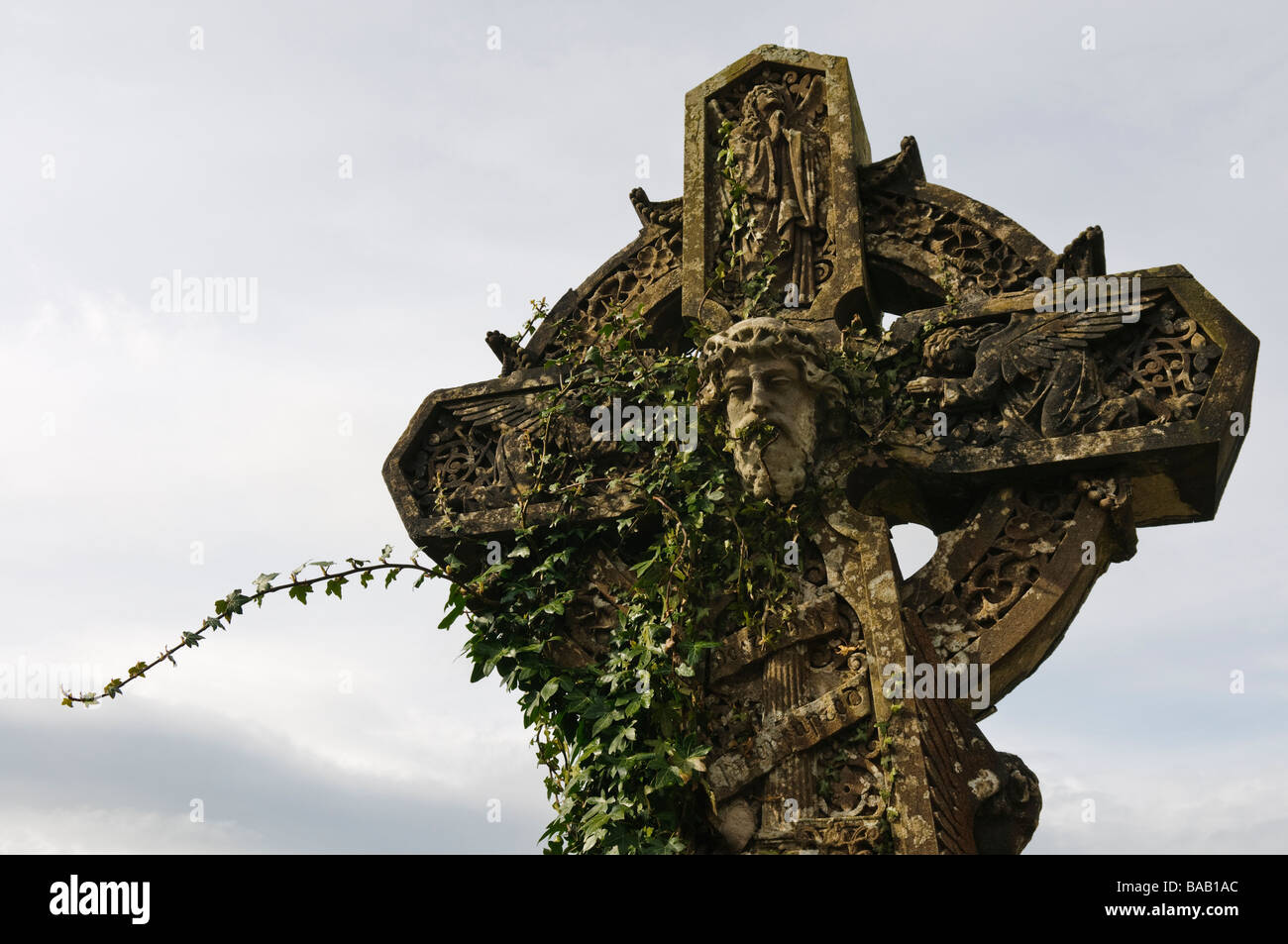 Ivy growing up an ornate celtic cross with face of Jesus carved in centre Stock Photo
