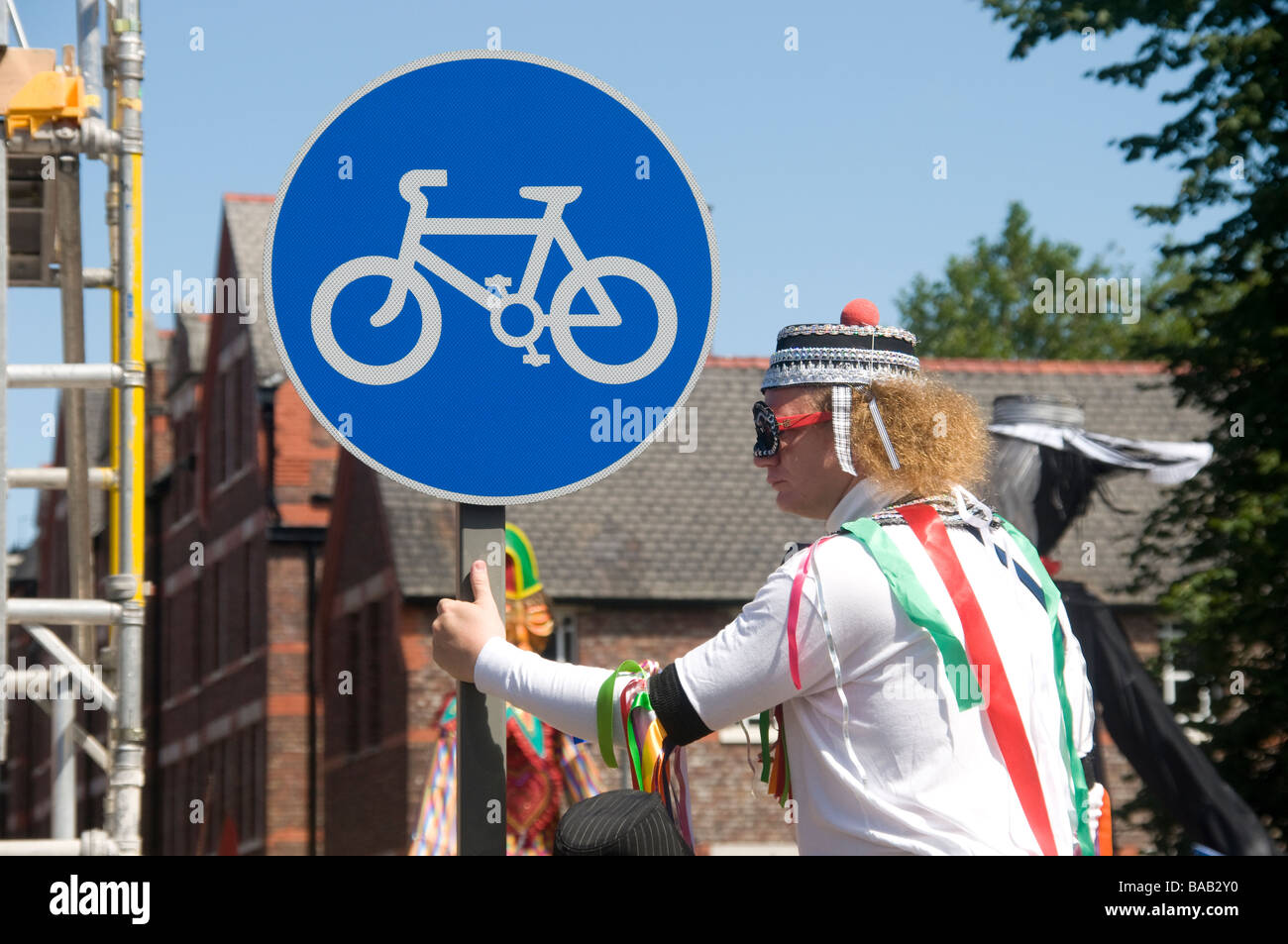 Stilt walker at carnival holds on to Cycling Permitted road sign Stock Photo