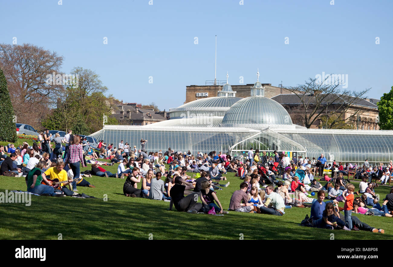 Small groups of people on a lawn in front of the Kibble Palace in Glasgow's Botanic Gardens, enjoying a sunny April day. Stock Photo