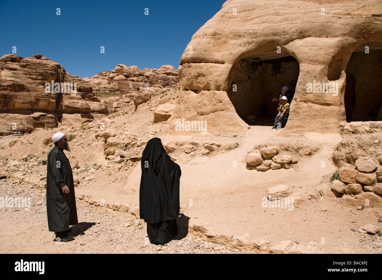 A Muslim family wandering in the rock cut tombs at the entrance to the ancient Nabatean city of Petra Jordan Stock Photo