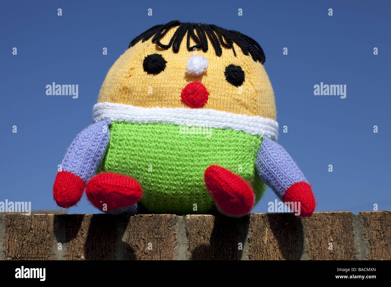 A Humpty Dumpty soft toy  sat on the wall with a blue sky background. Stock Photo