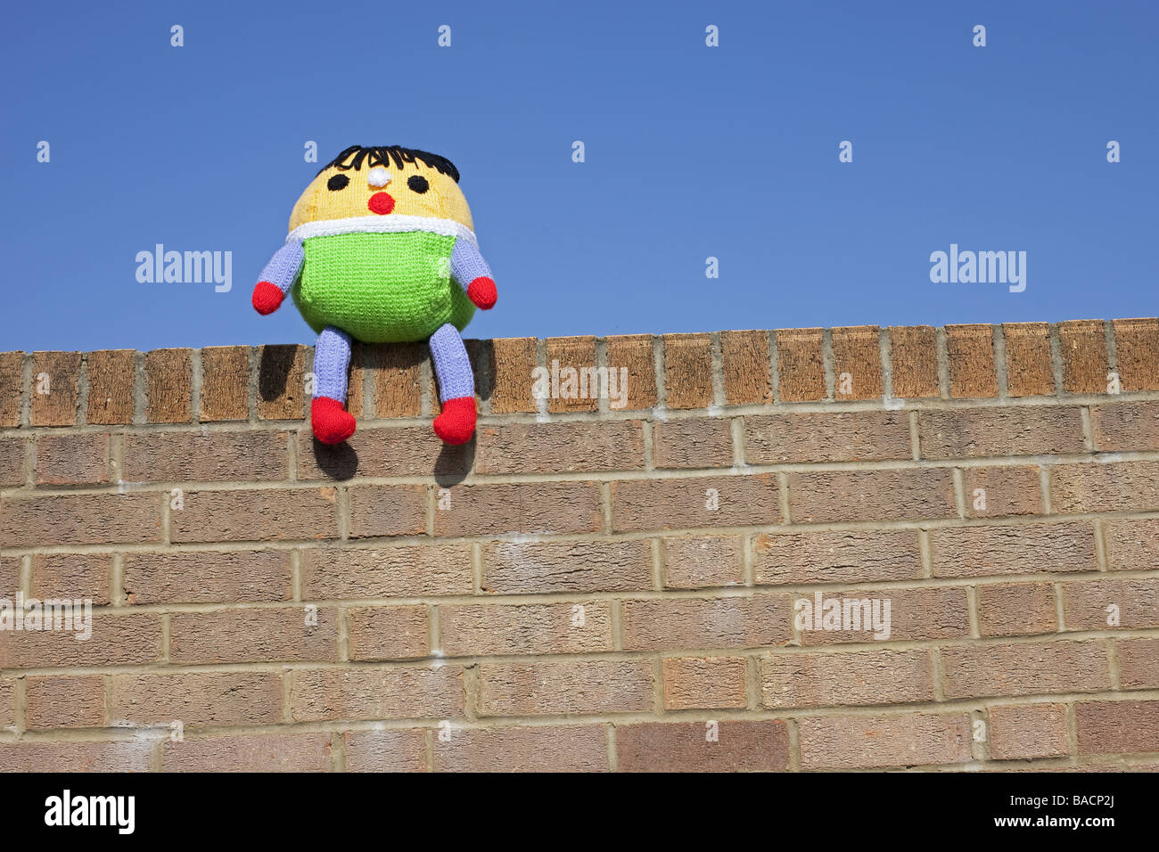 A Humpty Dumpty soft toy  sat on the wall with a blue sky background. Stock Photo