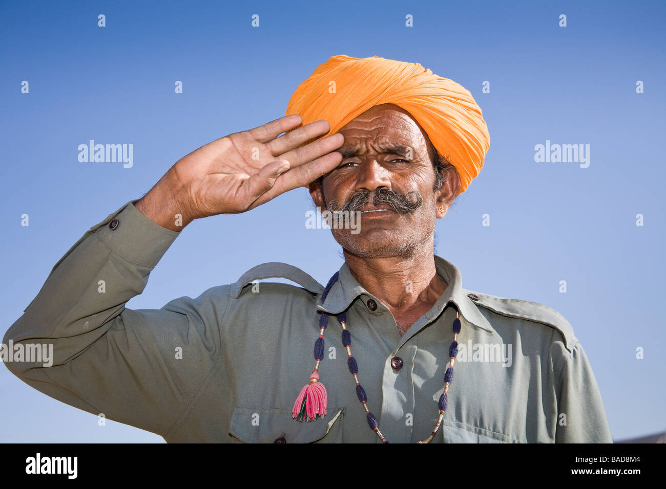 Man wearing a colourful saffron turban and saluting at Osian Camel Camp, Osian, Rajasthan, India Stock Photo