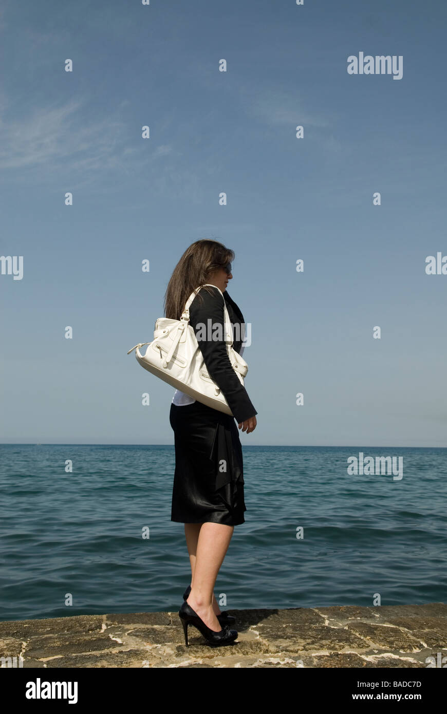 Business woman standing by the sea carrying a handbag Stock Photo