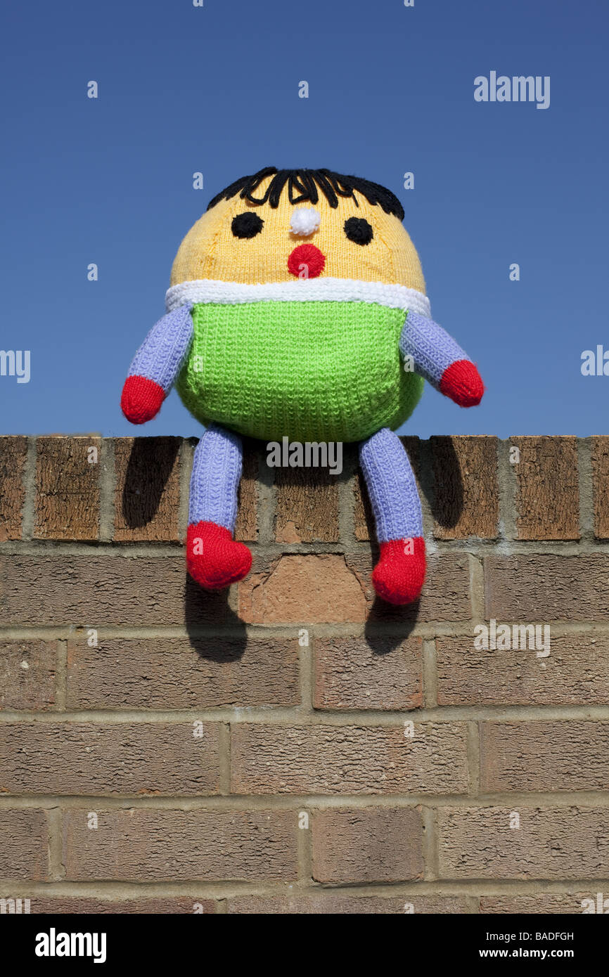 A Humpty Dumpty soft toy  sat on the wall with a blue sky background. Stock Photo