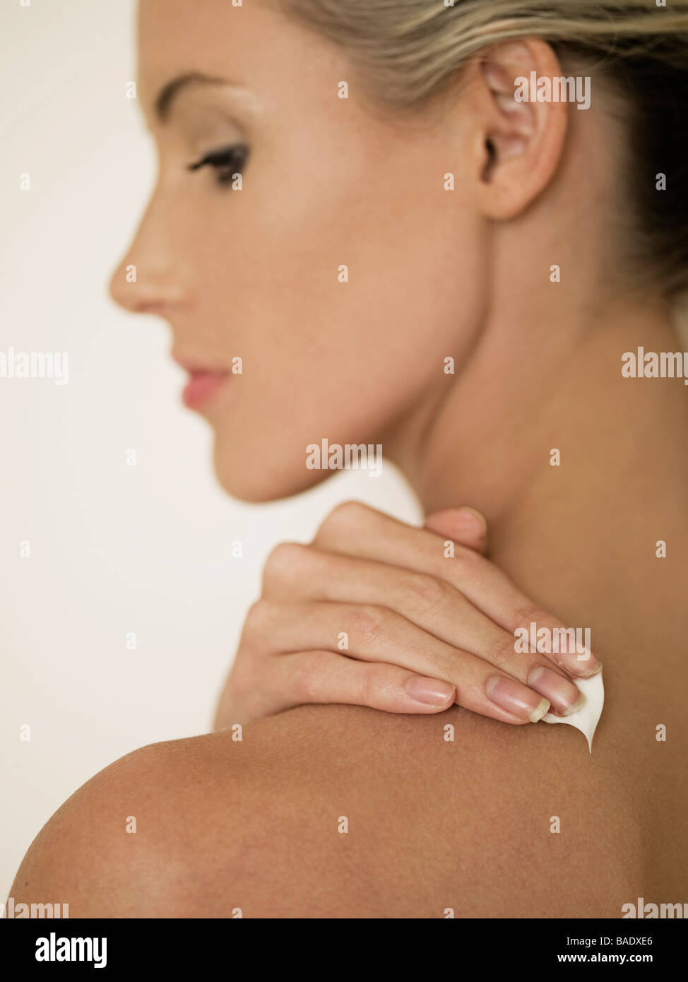 female face in profile rubbing cream into shoulder Stock Photo