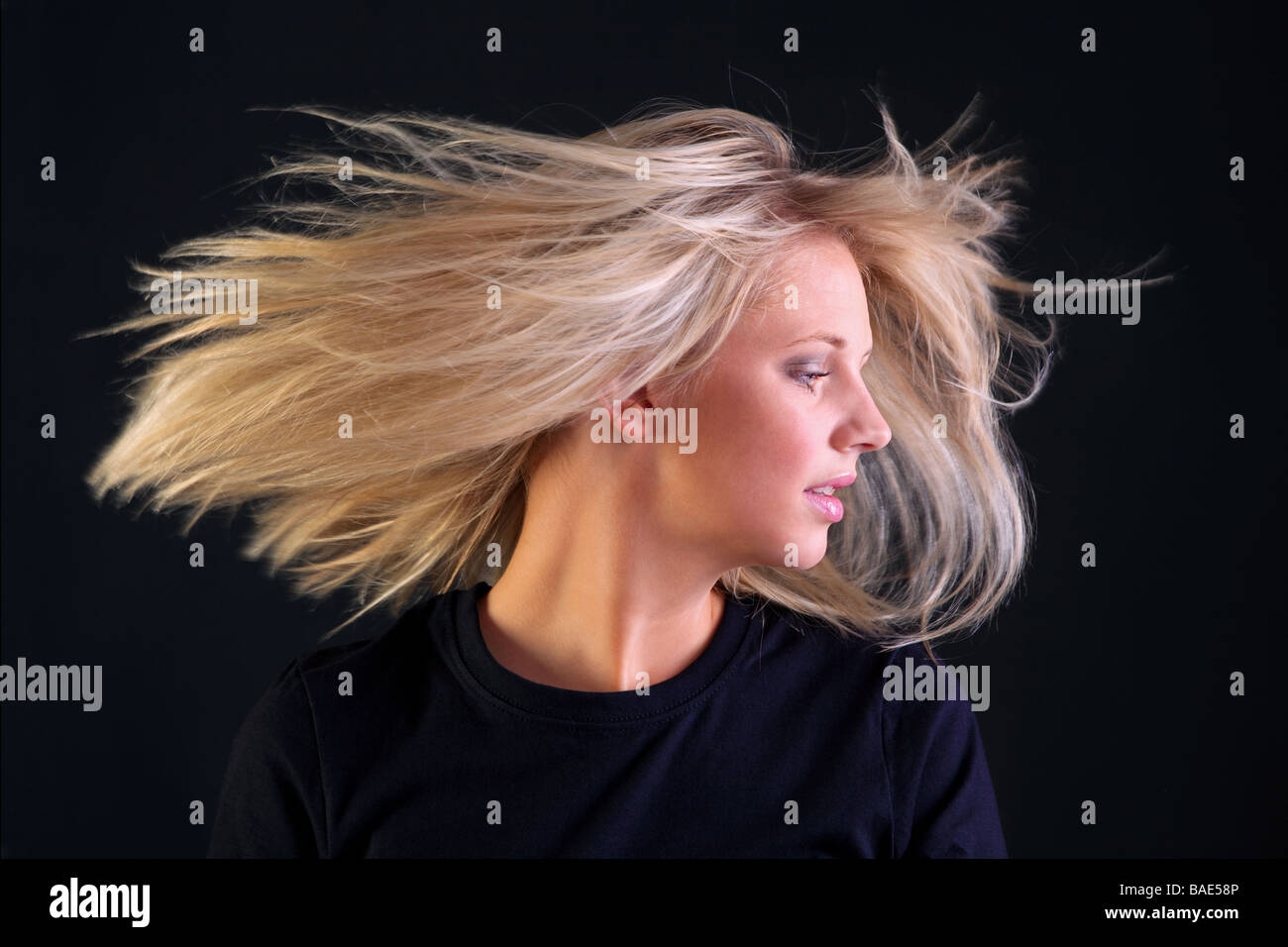 A beautful young woman with long blonde hairstyle turning her head so her hair flows black background Stock Photo