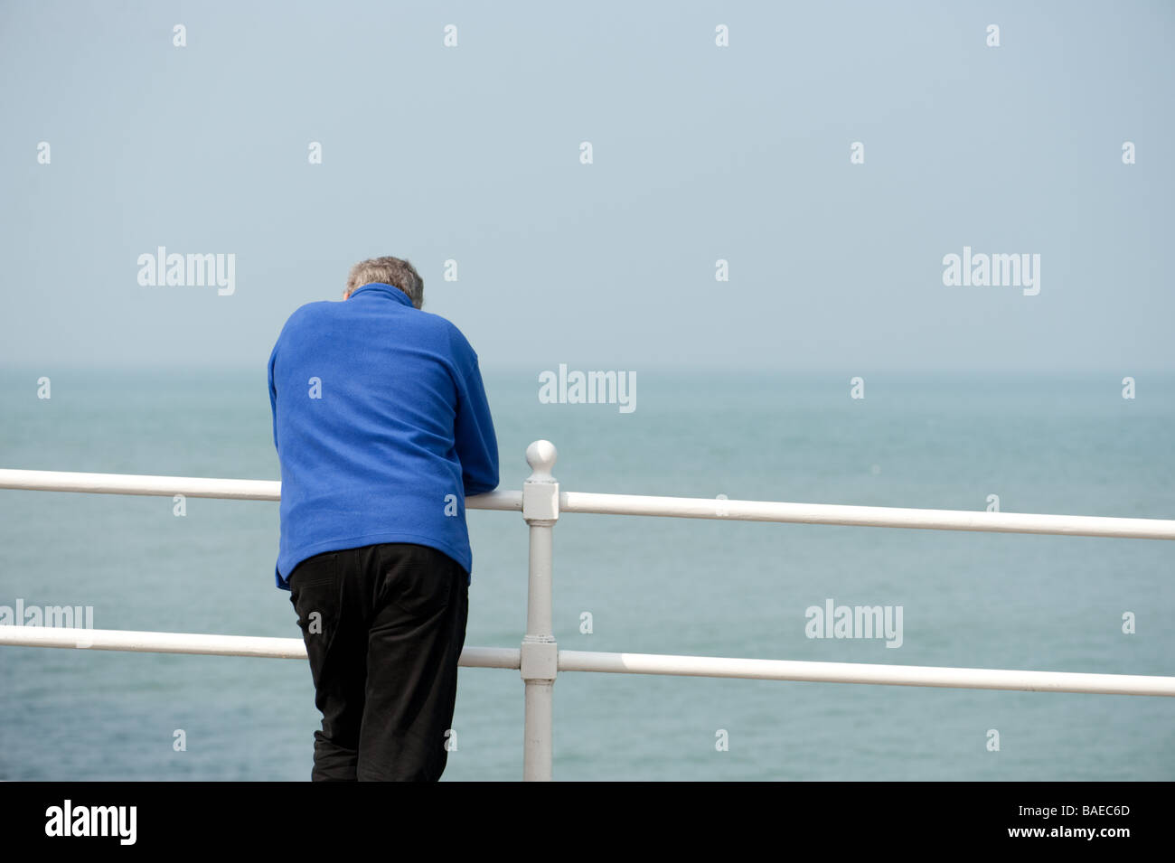 A middle aged man wearing a blue jacket leaning on the railings on the promenade at Aberystwyth wales UK, summer afternoon Stock Photo
