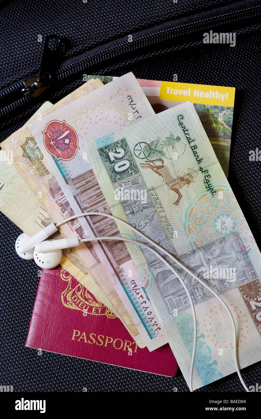 Close up of a British passport, foreign currency, travel health card and mp3 player headphones on top of a suitcase Stock Photo
