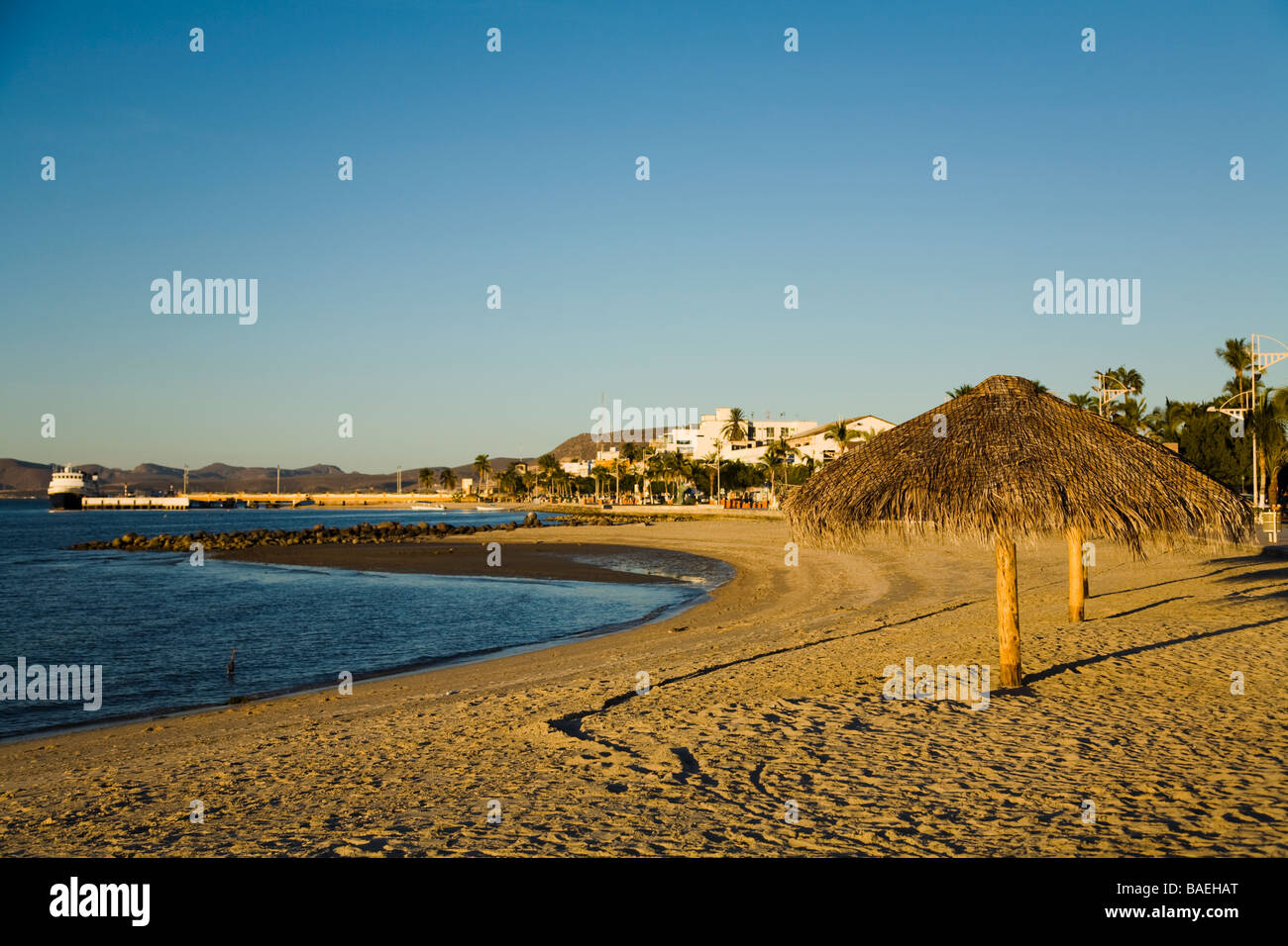 MEXICO La Paz Palapa thatched umbrellas on beach along bay city buildings and mountains in distance Stock Photo