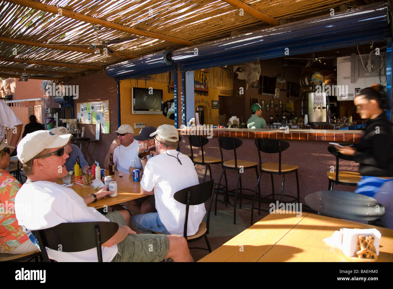 MEXICO Los Barriles American men wearing baseball caps eat at table in Tio Pablos restaurant bartender and waitress Stock Photo