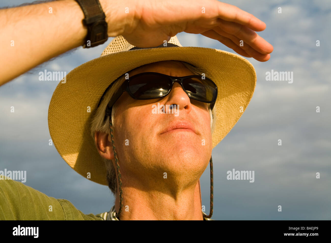 MEXICO Todos Santos Middle aged Caucasian male wearing straw hat and sunglasses look into distance shield eyes from sun by hand Stock Photo