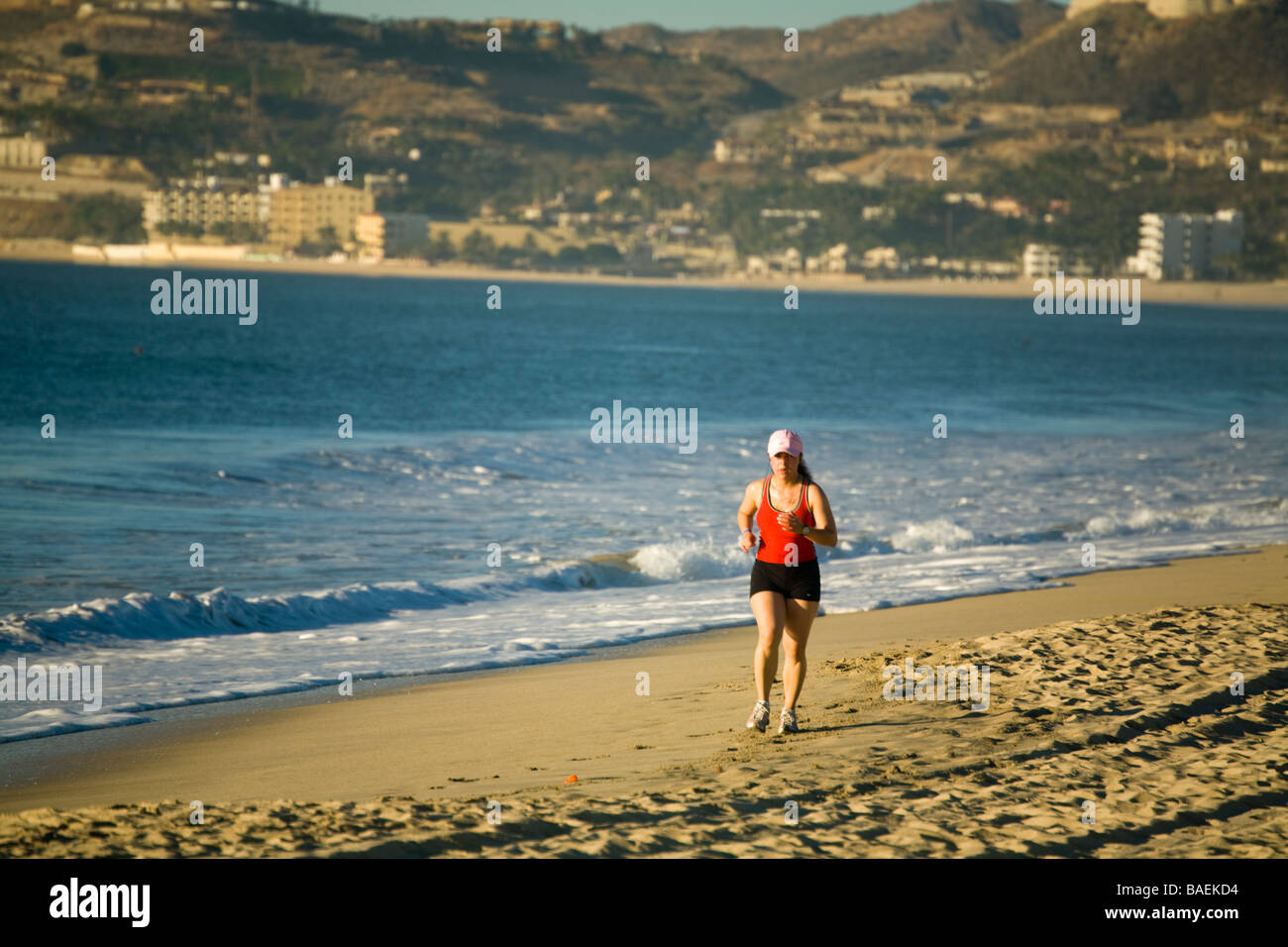 MEXICO San Jose del Cabo Young woman running on beach in early morning buildings alone shore in distance waters of Sea Cortez Stock Photo