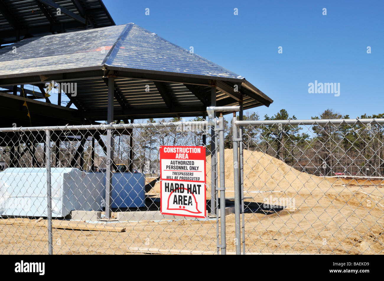 [Construction site] with metal frame building [chain link fence] and [warning sign] for 'hard hat area' Stock Photo