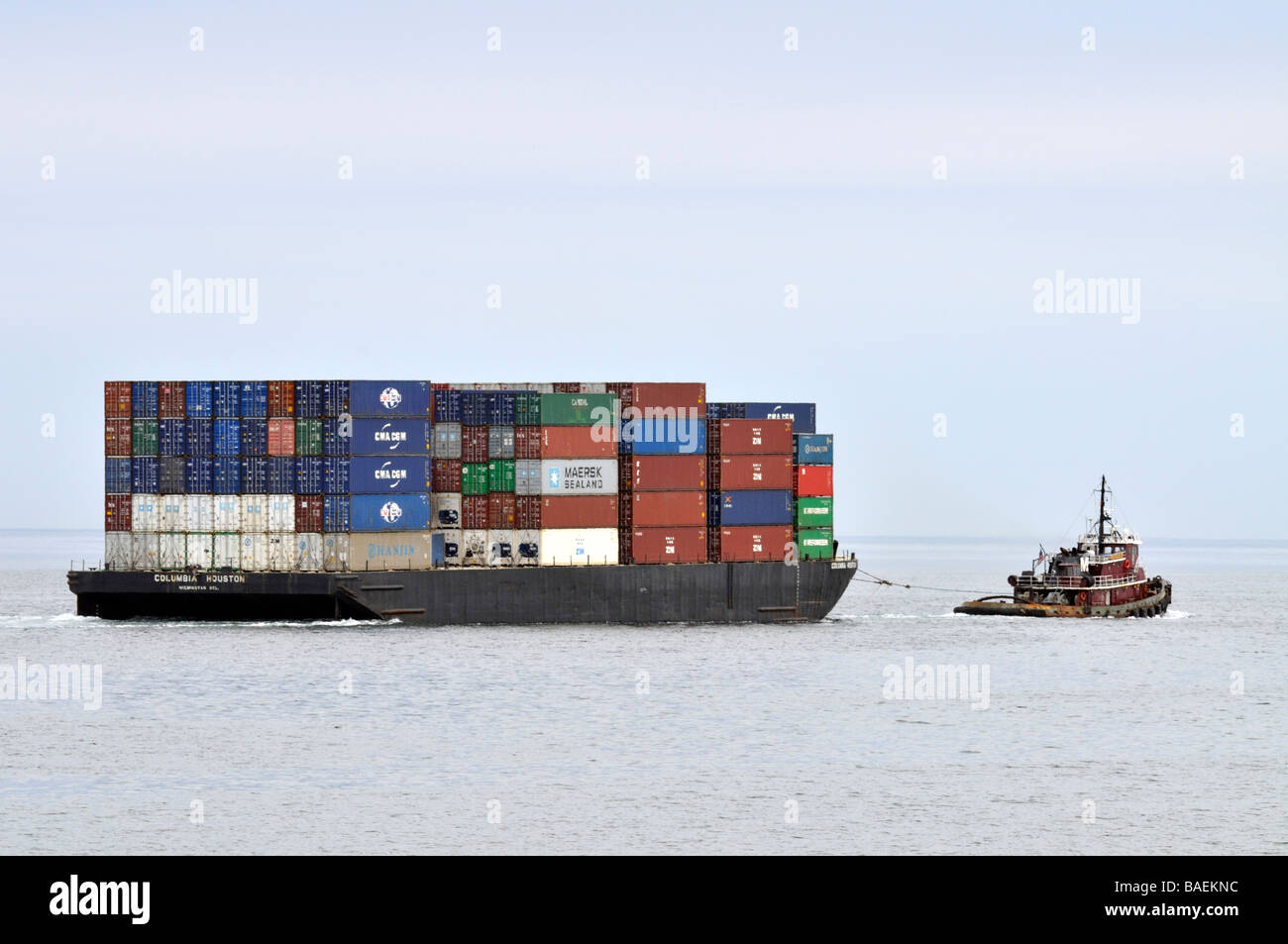 Tugboat pulling barge loaded with shipping containers at sea Stock Photo