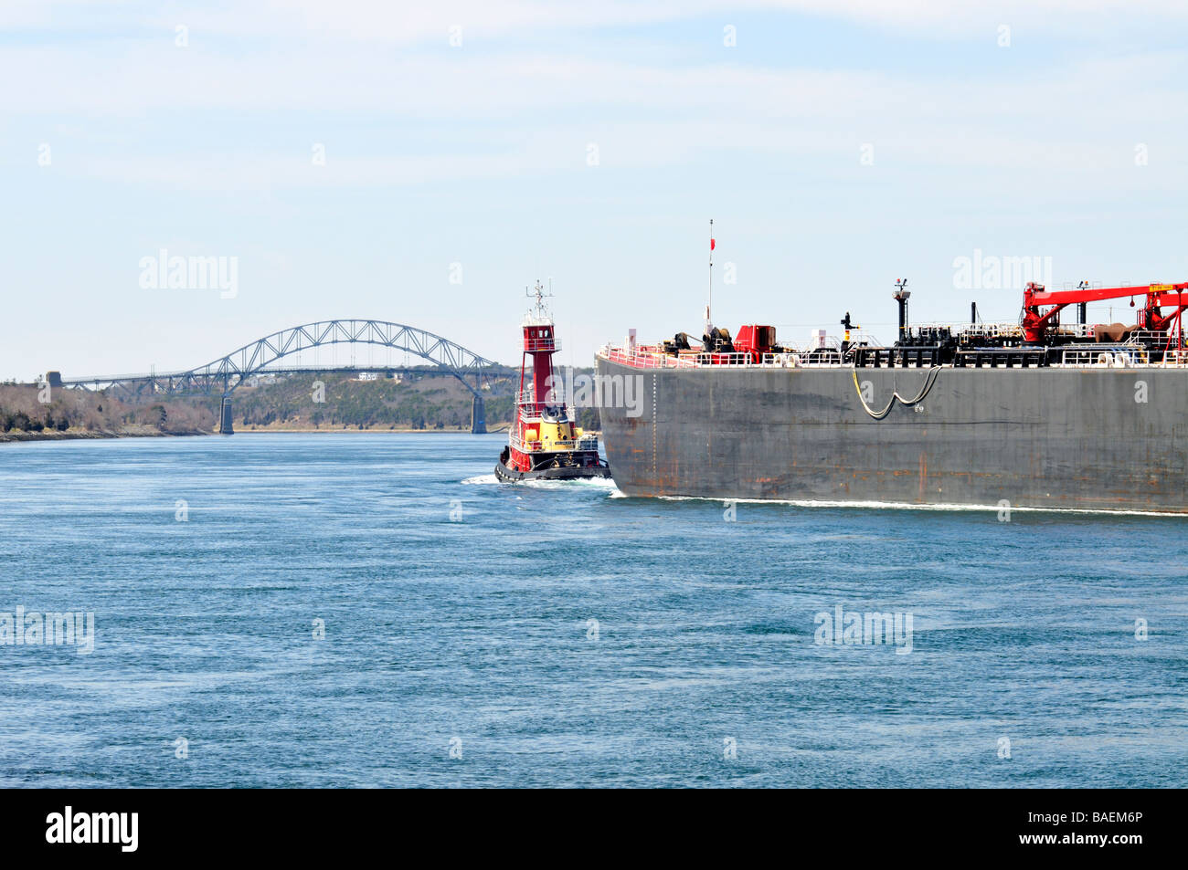 Red tugboat towing fuel oil barge through Cape Cod Canal towards Sagamore Bridge Stock Photo