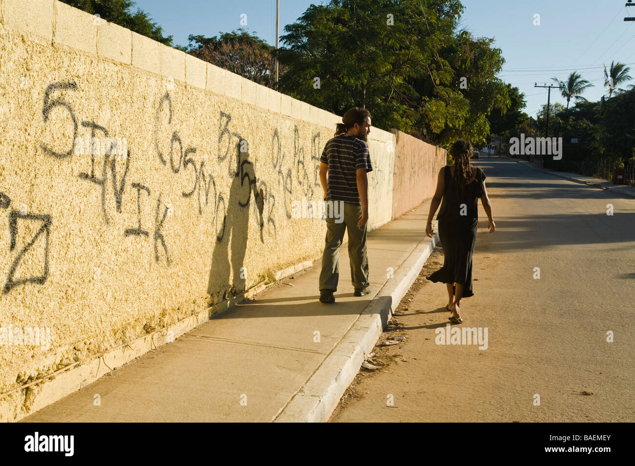 MEXICO La Playita Young adult couple walk past graffiti painted with black spray paint on yellow wall in small Mexican town Stock Photo