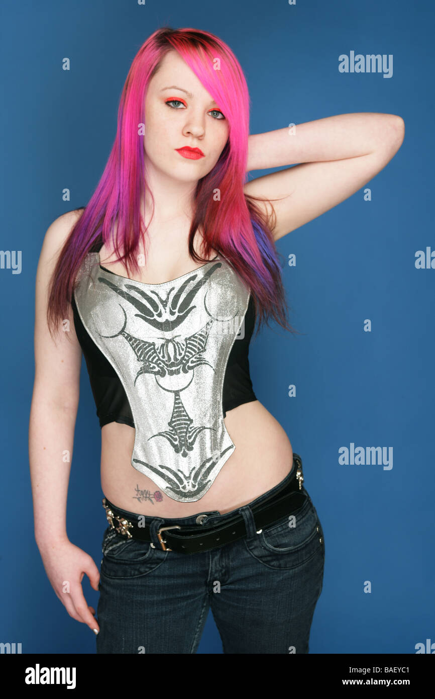 Young teen with bright pink hair red lips and pale skin standing with one hand behind her head. Stock Photo
