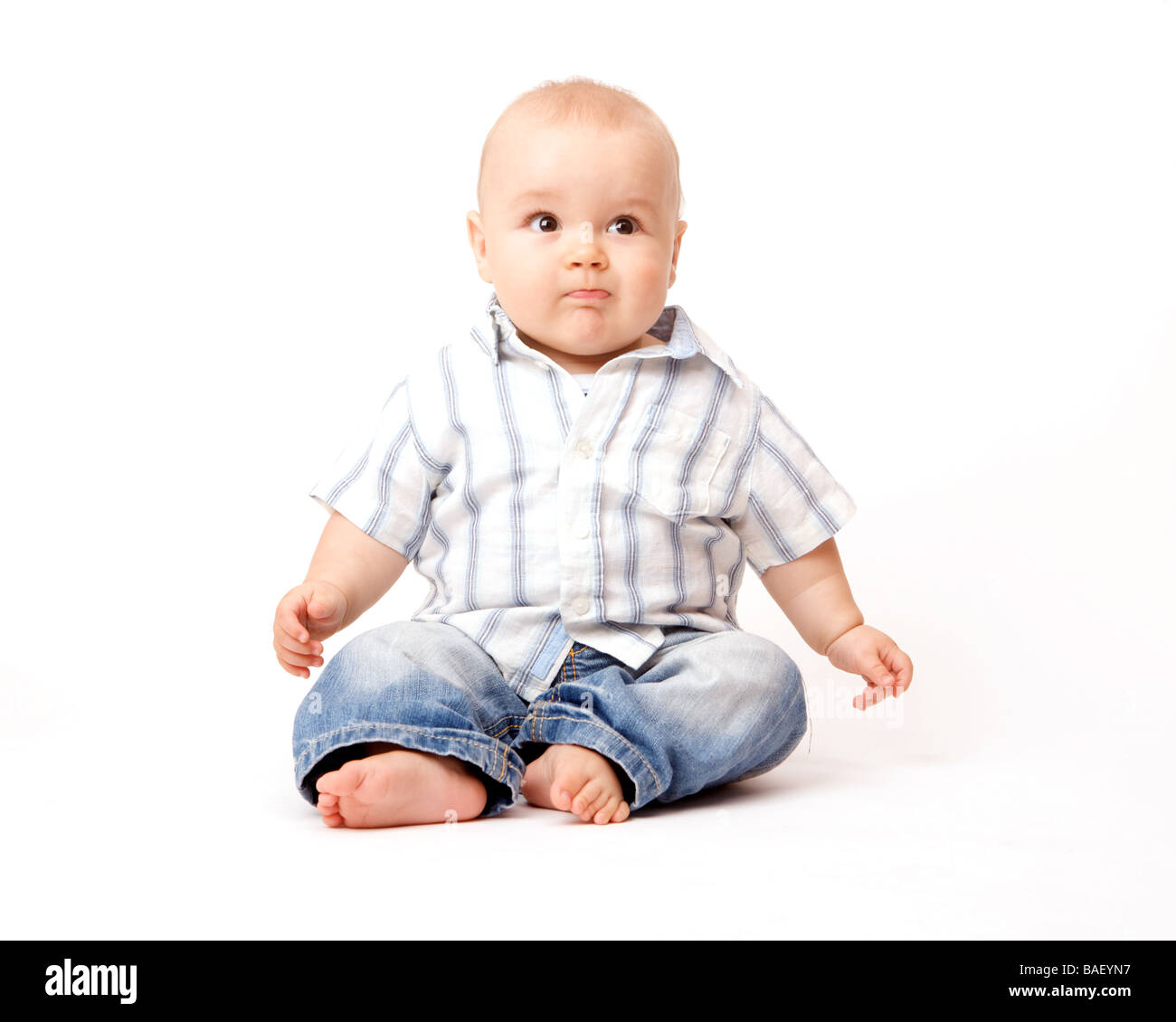 A baby sits on a white background with denims and a striped shirt Stock Photo