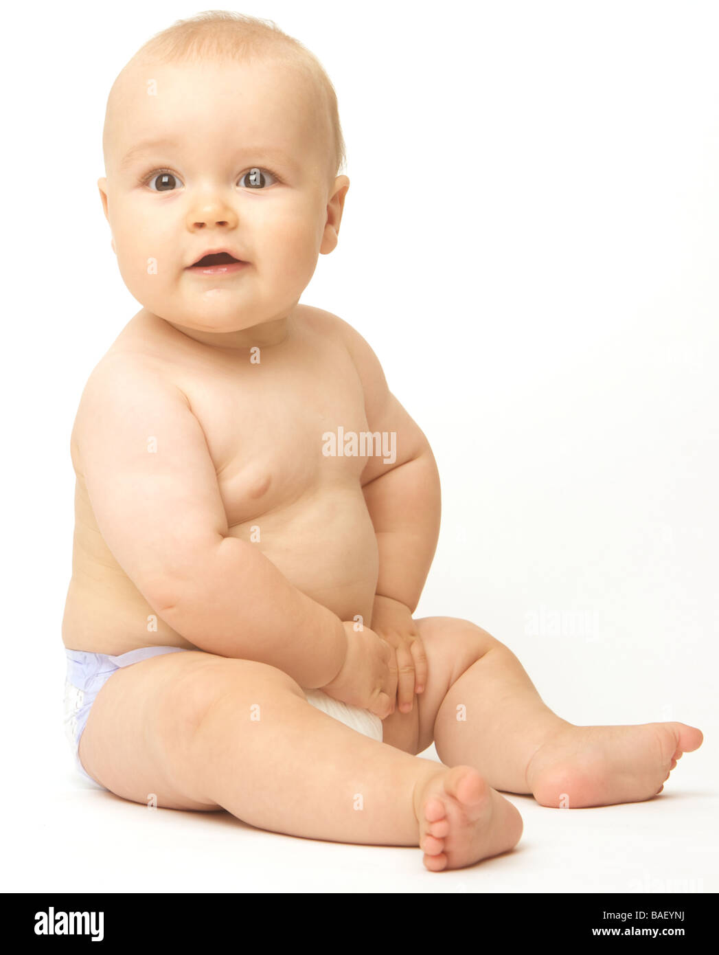 A baby sits against a white backdrop wearing a nappy Stock Photo