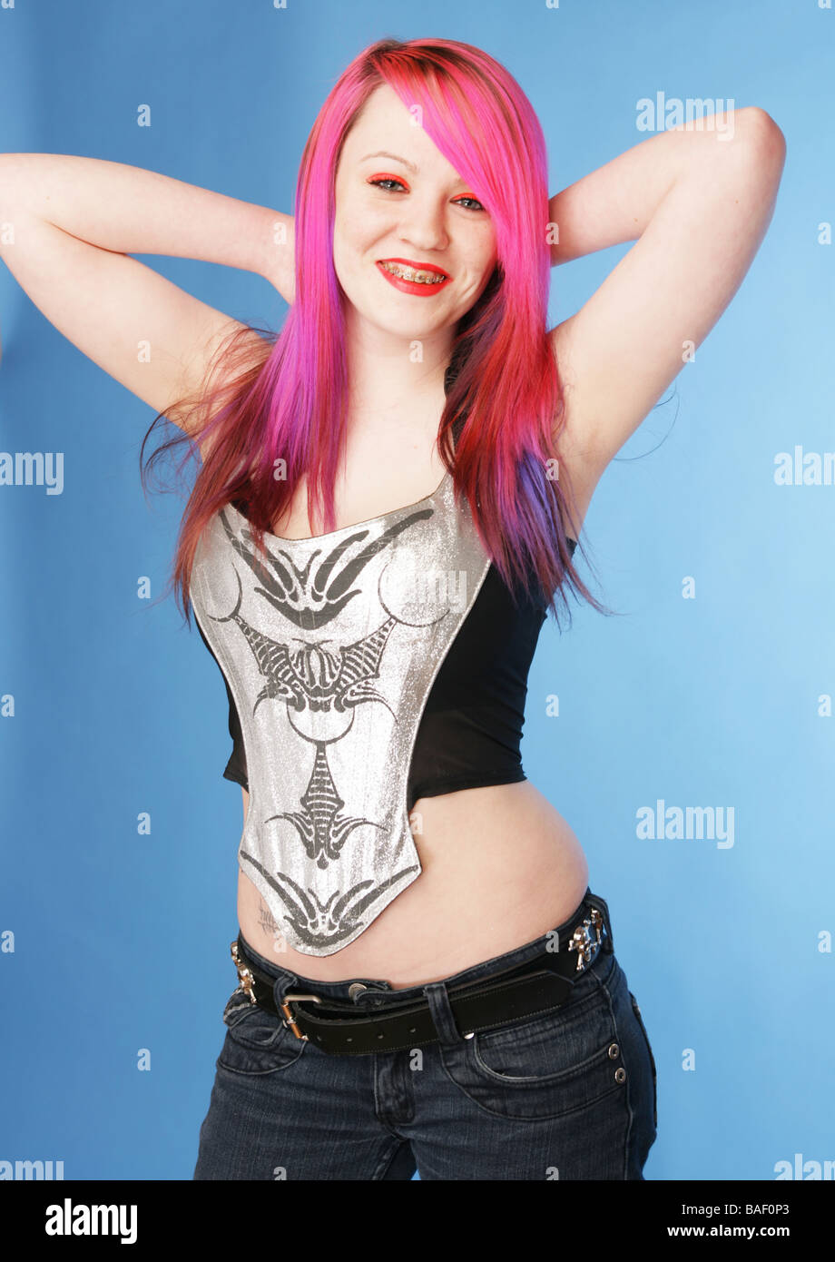 Young teen with bright pink hair red lips and pale skin smiling ,standing holding her hands behind her head Stock Photo