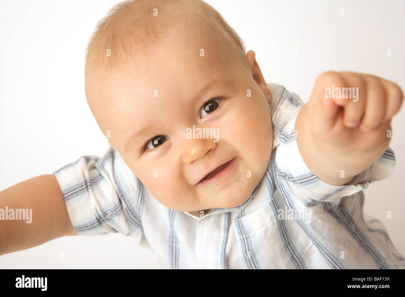 A smiling baby wearing a shirt reaches up to camera Stock Photo