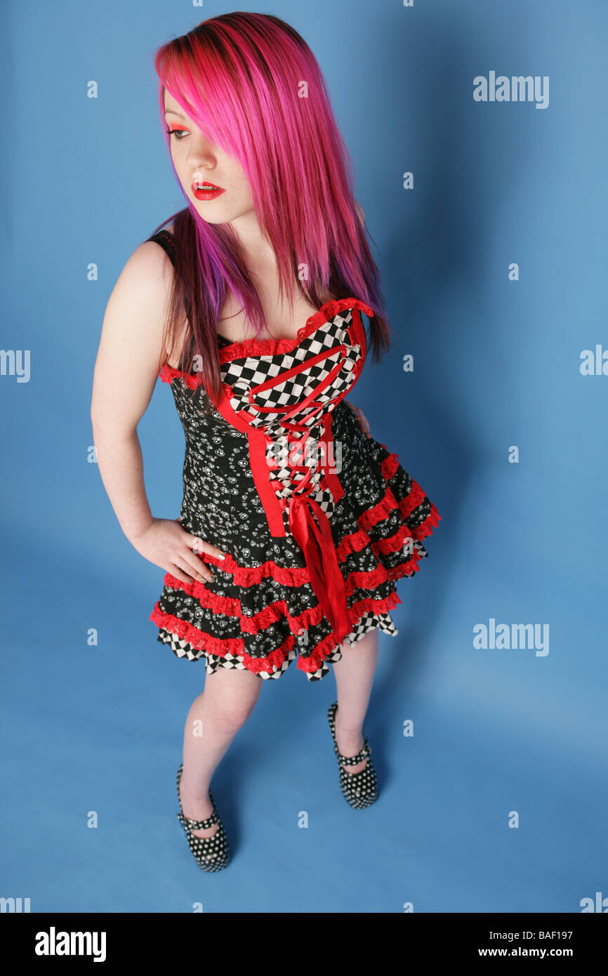 Full length Portrait of a beautiful teen girl with long pink hair pale skin and red lips wearing a red and black dress. Stock Photo