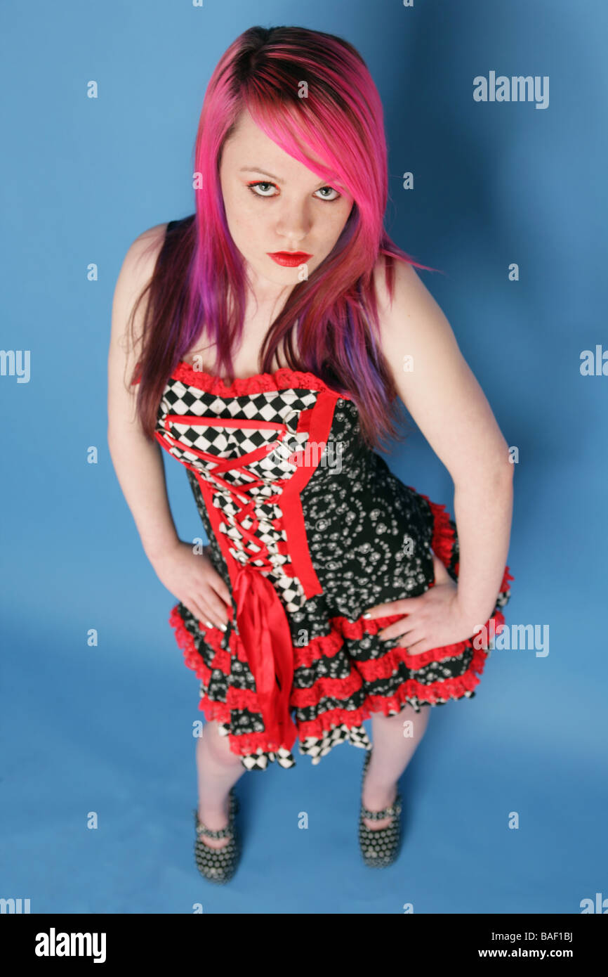 Full length Portrait of a beautiful teen girl with long pink hair pale skin and red lips wearing a red and black dress. Stock Photo