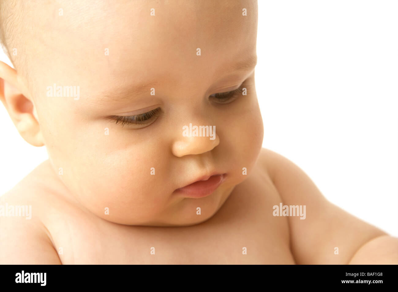 A baby looks downwards against a white backdrop Stock Photo