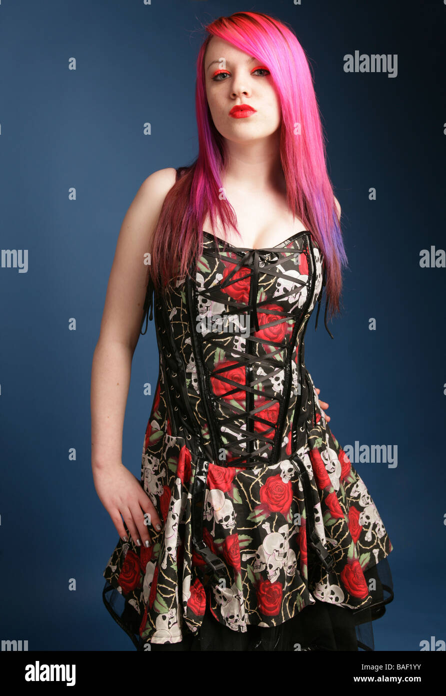 Alternative looking teen with bright pink hair red lips and pale skin standing with a hand on her hip Stock Photo